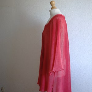 Puede incluir: Una t&uacute;nica de color rosa coral, ligera, transparente y de corte holgado con un dobladillo ligeramente asim&eacute;trico. La t&uacute;nica tiene un escote redondo y mangas cortas y anchas.