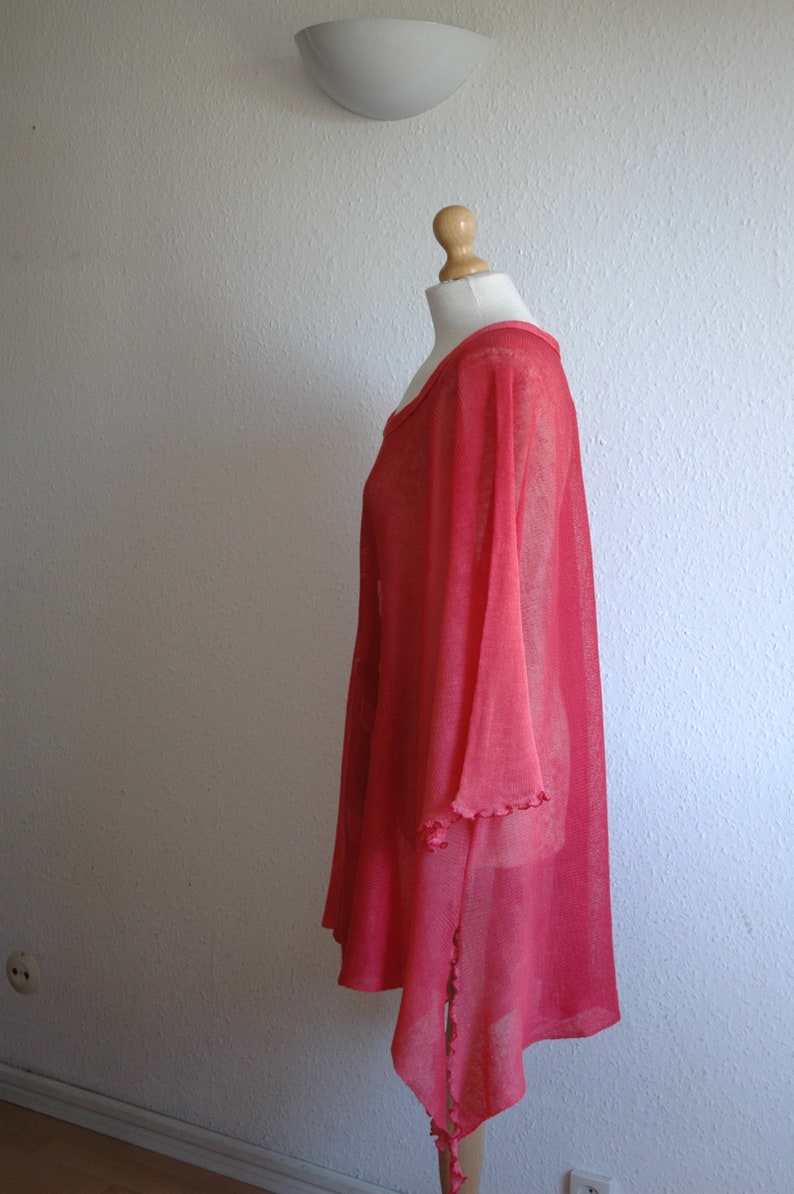 Puede incluir: Una t&uacute;nica de color rosa coral, ligera, transparente y de corte holgado con un dobladillo ligeramente asim&eacute;trico. La t&uacute;nica tiene un escote redondo y mangas cortas y anchas.