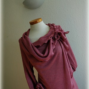 May include: A long-sleeved, mauve-colored sweater with a cowl neck and a large, ruffled flower detail on the shoulder.