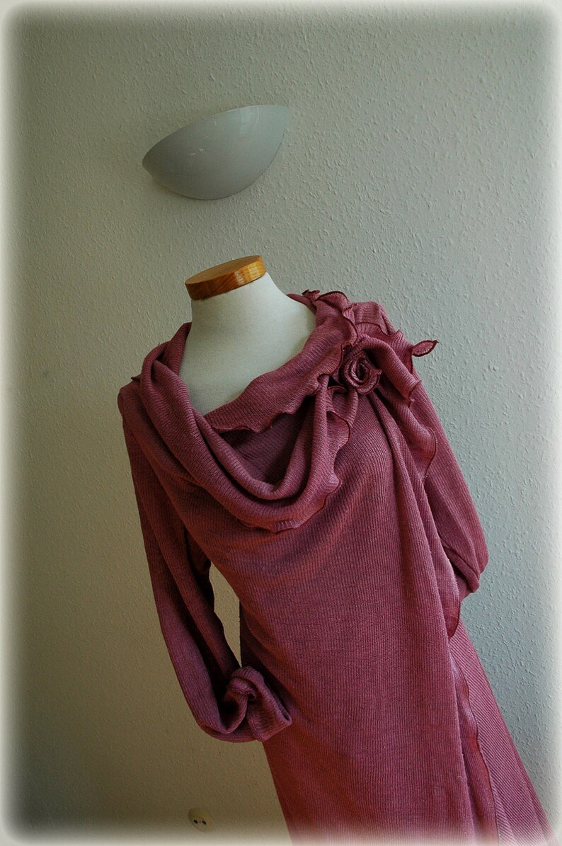 May include: A long-sleeved, mauve-colored sweater with a cowl neck and a large, ruffled flower detail on the shoulder.