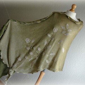 May include: A green shawl with a scalloped edge and white embroidered floral design.