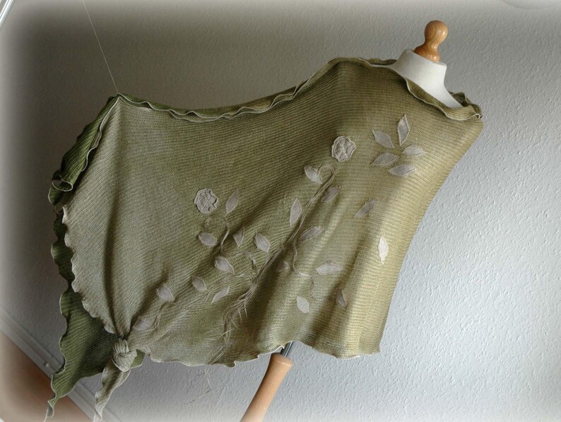 May include: A green shawl with a scalloped edge and white embroidered floral design.