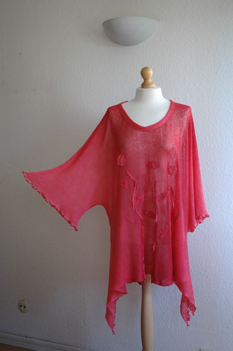 Puede incluir: Una blusa ligera y fluida de color coral, transparente, de corte holgado. La blusa presenta delicados bordados florales y un dobladillo ligeramente asim&eacute;trico.