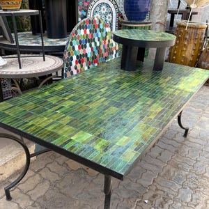 May include: A rectangular table with a green mosaic tile top and black metal legs. The table is surrounded by other decorative items, including vases and smaller tables. The mosaic tiles are various shades of green.