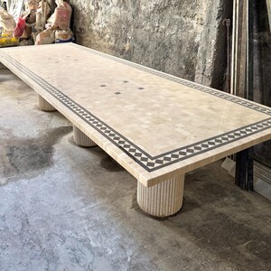 May include: A large rectangular mosaic table with a beige and black geometric border. The table is supported by four cylindrical legs. The table measures approximately 120 inches long.