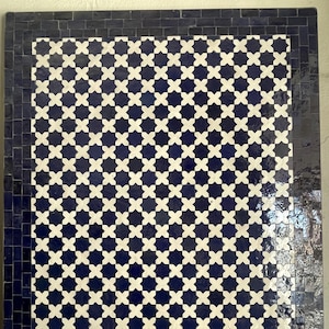 May include: A rectangular tile mosaic with a dark blue border and a repeating pattern of white star-like shapes on a dark blue background. The mosaic is made of small, square tiles.