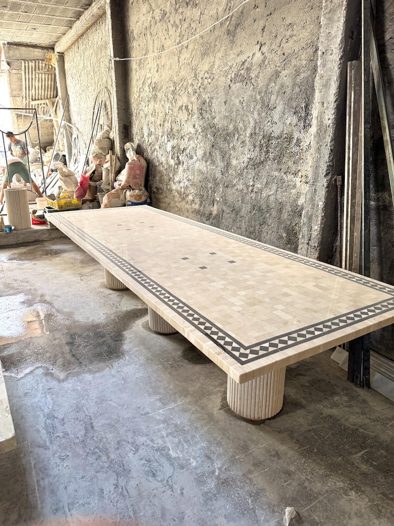 May include: A large rectangular mosaic table with a beige and black geometric border. The table is supported by four cylindrical legs. The table measures approximately 120 inches long.