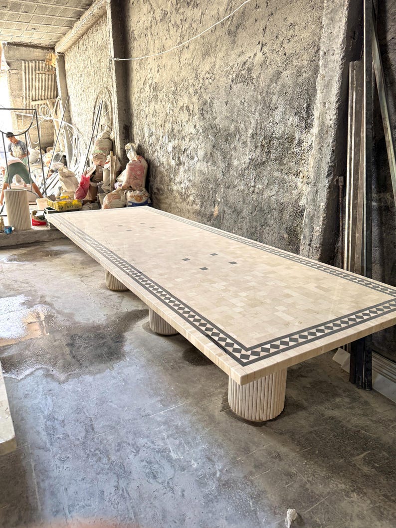 May include: A large rectangular mosaic table with a beige and black geometric border. The table is supported by four cylindrical legs. The table measures approximately 120 inches long.