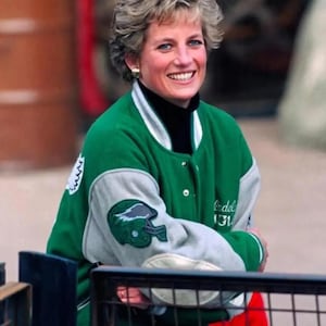 May include: A green and grey letterman jacket with a black turtleneck. The jacket features a football helmet patch on the sleeve and the word "bedel" and the number "131" on the sleeve.
