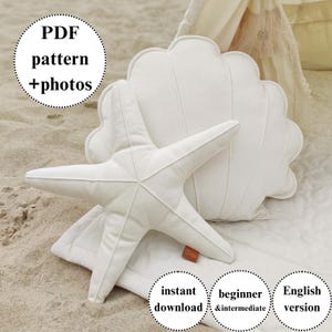Könnte beinhalten: Ein weißes Seesternkissen und ein weißes Muschelkissen werden auf einer weißen Oberfläche gezeigt. Das Seesternkissen hat fünf Zacken. Das Muschelkissen hat einen gewellten Rand. Der Text im Bild lautet "PDF pattern + photos", "instant download", "beginner & intermediate" und "English version".