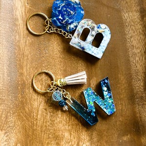 Llavero de resina azul brillante, dije para bolso o cartera con cadena dorada y detalles en azul, cuentas de colores o borla.