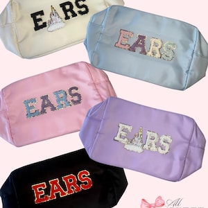 May include: Several rectangular cosmetic bags in shades of cream, light blue, pink, purple, and black. Each bag is adorned with the word "EARS" in a decorative font, with some featuring a castle graphic.