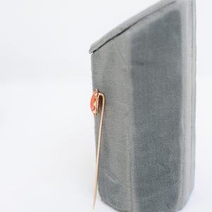 May include: A gold pin with a red coral stone set in a gold frame. The pin is on a gray velvet display stand.
