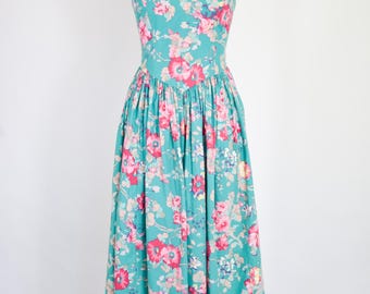May include: A sleeveless midi dress in a teal green color featuring a vibrant floral pattern with pink, red, and white blossoms. The dress has a fitted bodice with a V-neckline and a gathered, full skirt that falls below the knees.