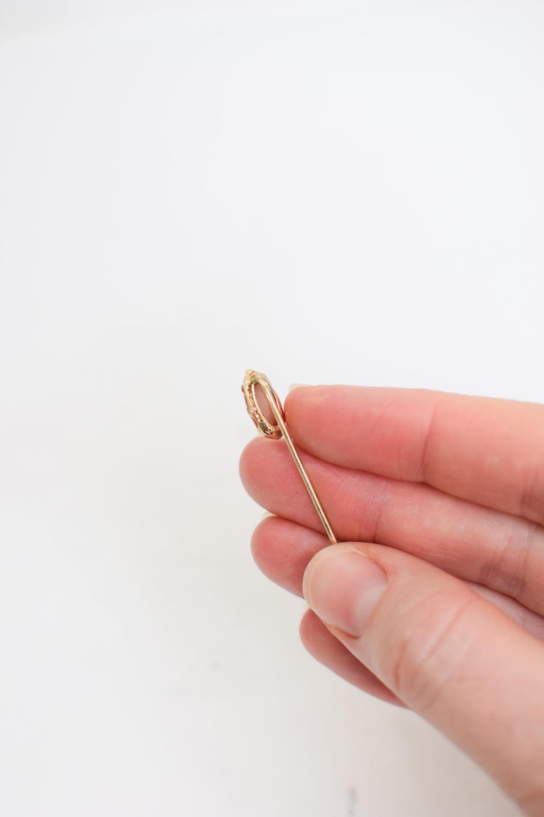 May include: A gold safety pin with a decorative loop at the top.