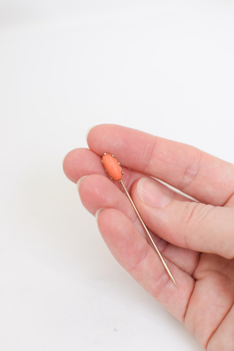 May include: A gold pin with a coral oval cabochon.