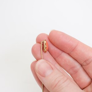 May include: A gold-toned tie tack with a coral-colored oval stone.