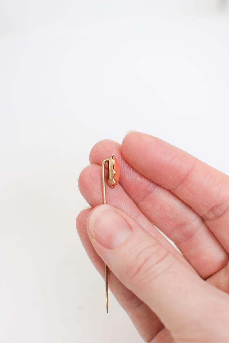May include: A gold-toned tie tack with a coral-colored oval stone.