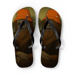 May include: Pair of flip-flops featuring a humorous design. Each flip-flop displays a Bigfoot-like figure wearing an orange bucket hat, reminiscent of the Mona Lisa. The background has a landscape scene, and the straps are black.