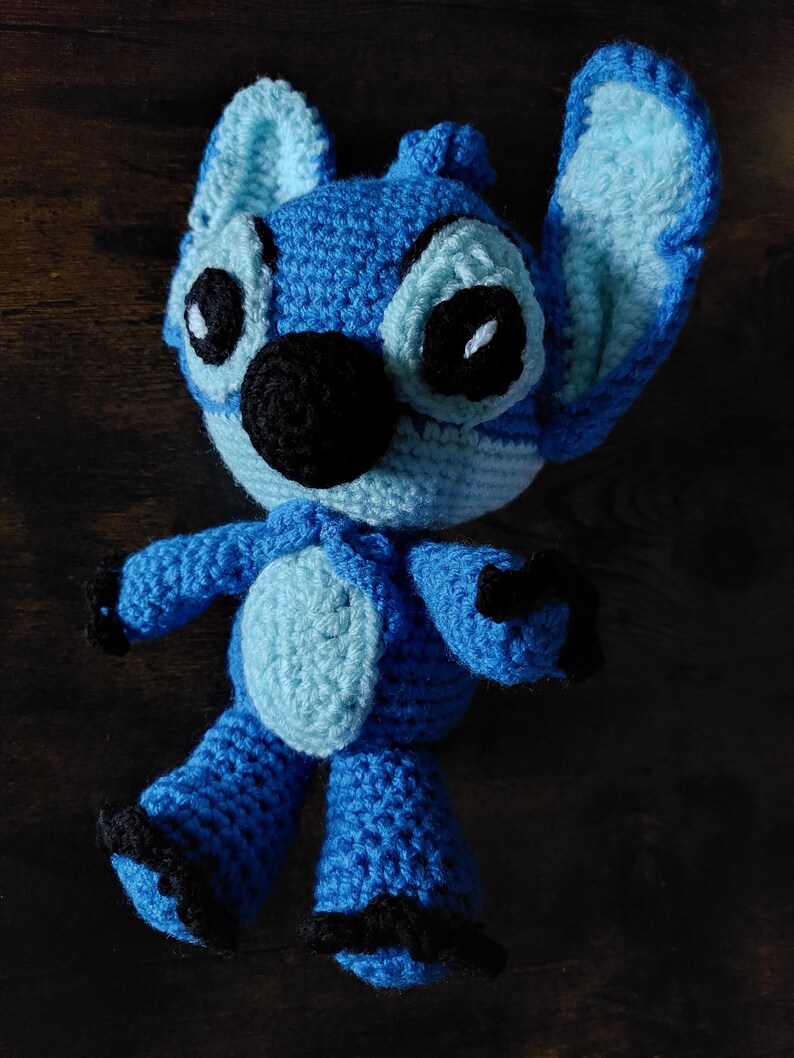 Puede incluir: Mu&ntilde;eco Stitch azul hecho a mano con ganchillo y detalles en azul claro. El mu&ntilde;eco tiene grandes ojos negros, una nariz negra y garras negras. Las orejas son grandes y est&aacute;n erguidas. Es un personaje popular de Disney.
