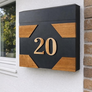 Könnte beinhalten: Ein rechteckiger Wandbriefkasten mit mattschwarzer Oberfläche, vier hölzernen Eckakzenten und der Zahl 20 in großen Holzlettern auf der Vorderseite. Das Design kombiniert einen dunklen Metallrahmen mit Elementen aus natürlichem Holz.