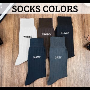 May include: Image of five pairs of ribbed dress socks in various colors: white, brown, black, navy, and grey. The socks are displayed on a wooden surface, with the words "SOCKS COLORS" at the top.