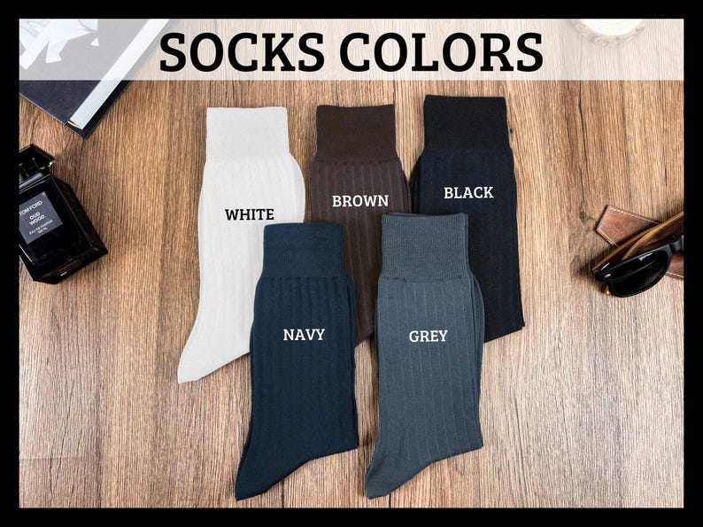 May include: Image of five pairs of ribbed dress socks in various colors: white, brown, black, navy, and grey. The socks are displayed on a wooden surface, with the words "SOCKS COLORS" at the top.