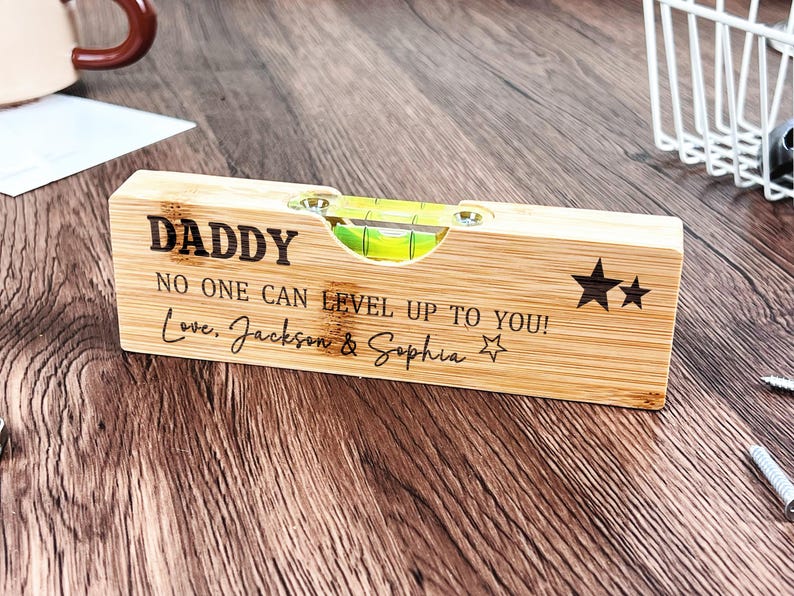 May include: A wooden level with the word "DADDY" engraved on it, along with the message "NO ONE CAN LEVEL UP TO YOU! Love, Jackson & Sophia." The level has a bubble vial and star graphics.