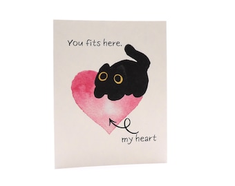 May include: A greeting card featuring a watercolor pink heart and a black cat with large yellow eyes. The text reads You fits here. above the cat and my heart below the heart with an arrow pointing to it. The background is a plain off-white color.