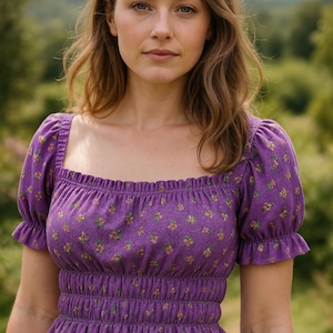 Puede incluir: Una blusa morada con estampado floral, con cuello cuadrado y mangas cortas con volantes. La blusa tiene cintura fruncida y está hecha de una tela suave. El diseño floral incluye flores amarillas, naranjas y rosas. El fondo es un paisaje verde borroso.