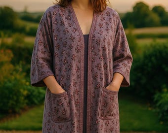 May include: A long, open-front robe in a muted purple hue, adorned with a delicate floral pattern in shades of pink and burgundy. The robe features three-quarter sleeves and two front pockets. The garment is worn over a matching dress.