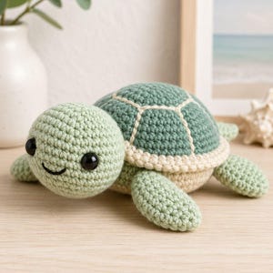 May include: A crochet turtle toy featuring a light green head and limbs, a dark green shell with cream-colored stitching, and black plastic eyes. The turtle has a simple embroidered smile and a cream-colored underside, crafted with visible yarn stitches.
