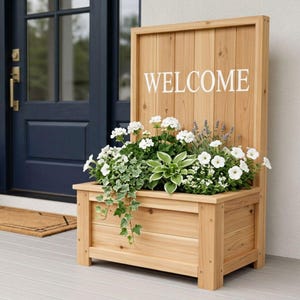Könnte beinhalten: Ein hölzerner Pflanzkasten mit dem Wort "WELCOME" in weißen Buchstaben. Der Pflanzkasten ist mit weißen Blumen, grünem Laub und Efeu gefüllt. Die Kiste ist aus hellem Holz gefertigt und steht auf einer Veranda.