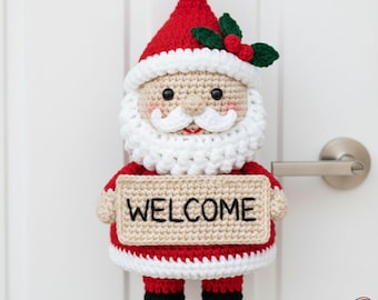 Può includere: Decorazione per porta a uncinetto a forma di Babbo Natale con cappello rosso, barba bianca e un cartello con la scritta "WELCOME". Babbo Natale ha un abito rosso e bianco con stivali neri ed è decorato con agrifoglio e bacche.
