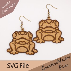 May include: A pair of wooden frog earrings with bronze-colored ear wires. The earrings are laser-cut with a detailed frog design. The image also includes the text "Laser Cut File" and "SVG File".