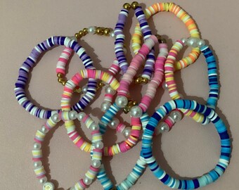 May include: A collection of colorful beaded bracelets in various designs. The bracelets feature a mix of pastel and vibrant colors, including pink, blue, yellow, and white. Some bracelets incorporate faux pearls and gold-colored beads.