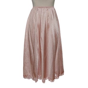 May include: A pale pink, full-length slip skirt with a delicate lace trim at the hem. The skirt has a subtle sheen and a gathered waistline. The fabric appears lightweight and flowing, suitable for layering or wearing on its own.