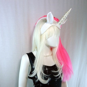 May include: A white unicorn headband with a pink hair extension. The headband has a white horn and ears.