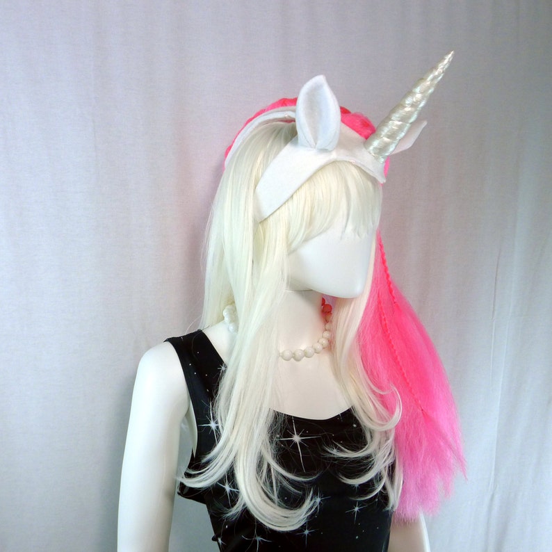 May include: A white unicorn headband with a pink hair extension. The headband has a white horn and ears.
