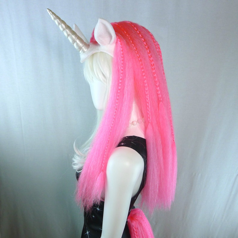 May include: A white unicorn headband with a pink and white wig. The wig is styled in long braids.
