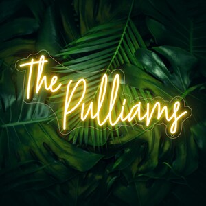 May include: A neon sign in a cursive font that reads "The Pulliams" in bright yellow against a backdrop of lush green tropical leaves. The sign is outlined with a clear border and has small holes for mounting.