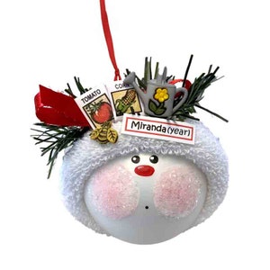 A delightful Gardening Gift Christmas Ornament featuring seeds, a bee, and a watering can. Perfect for gardeners and nature enthusiasts. Ideal for bringing the beauty of the garden to your holiday decorations.