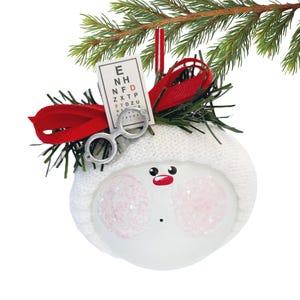 Puede incluir: Adorno navideño con forma de muñeco de nieve con gorro blanco de punto, mejillas rosas, nariz roja y boca negra pequeña. Incluye una tabla optométrica en miniatura y gafas plateadas.