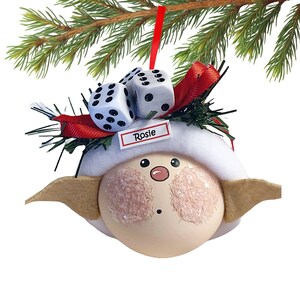 Puede incluir: Adorno navide&ntilde;o caprichoso con una cara redonda, mejillas rosadas, un sombrero blanco y orejas beige. Dos dados blancos con puntos negros est&aacute;n encima del sombrero, con una cinta roja y el nombre "Rosie".