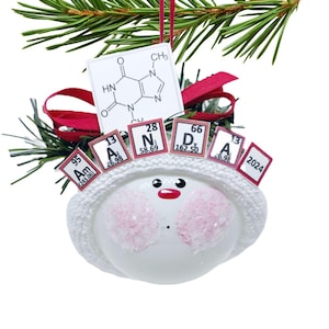 May include: A white snowman Christmas ornament with a knitted hat, pink cheeks, and a red nose. The ornament has periodic table elements and a chemical structure diagram. The year 2024 is also displayed.
