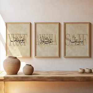 Könnte beinhalten: Drei gerahmte arabische Kalligraphie-Poster mit Namen in schwarzer Schrift auf beigem Hintergrund. Die Rahmen sind hellbraun. Der Text "PERSONALISIERTE ARABISCHE KALLIGRAPHIE POSTER" wird rechts angezeigt. Keramikvasen und kleine Schalen stehen auf einer Holzoberfläche.