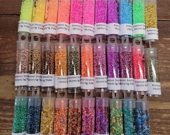 Może przedstawiać: Kolekcja małych, kolorowych szklanych koralików w przezroczystych plastikowych tubach. Każda tuba jest oznaczona nazwą marki "Forever Beading" i kodem produktu. Korale są ułożone w rzędach, z różnymi kolorami i wykończeniami.