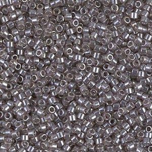 May include: A close-up shot of numerous small, cylindrical, silver-colored glass beads. The beads are densely packed together, creating a textured surface. Each bead has a small hole running through its center, and they reflect light, giving them a shiny appearance.