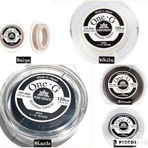 May include: Four spools of beading thread in beige, white, brown, and black. Each spool has a label that says "One.G TOHO BEADS Beading Thread" and includes the thread's dtex, material, and yardage.