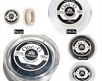 May include: Four spools of beading thread in beige, white, brown, and black. Each spool has a label that says "One.G TOHO BEADS Beading Thread" and includes the thread's dtex, material, and yardage.